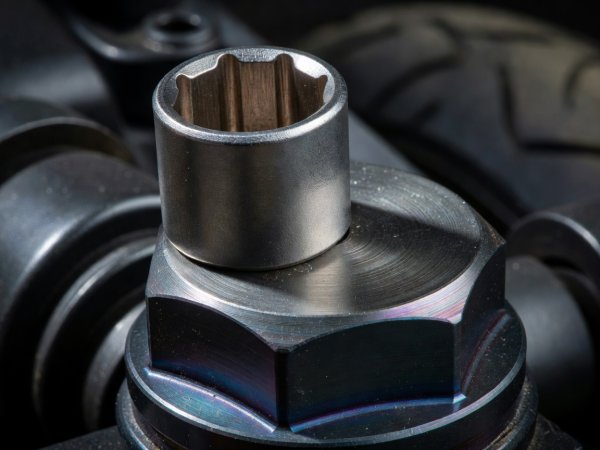Close-up of a six-point flank-drive socket engaging the flats of an anodized aluminum motorcycle axle nut
